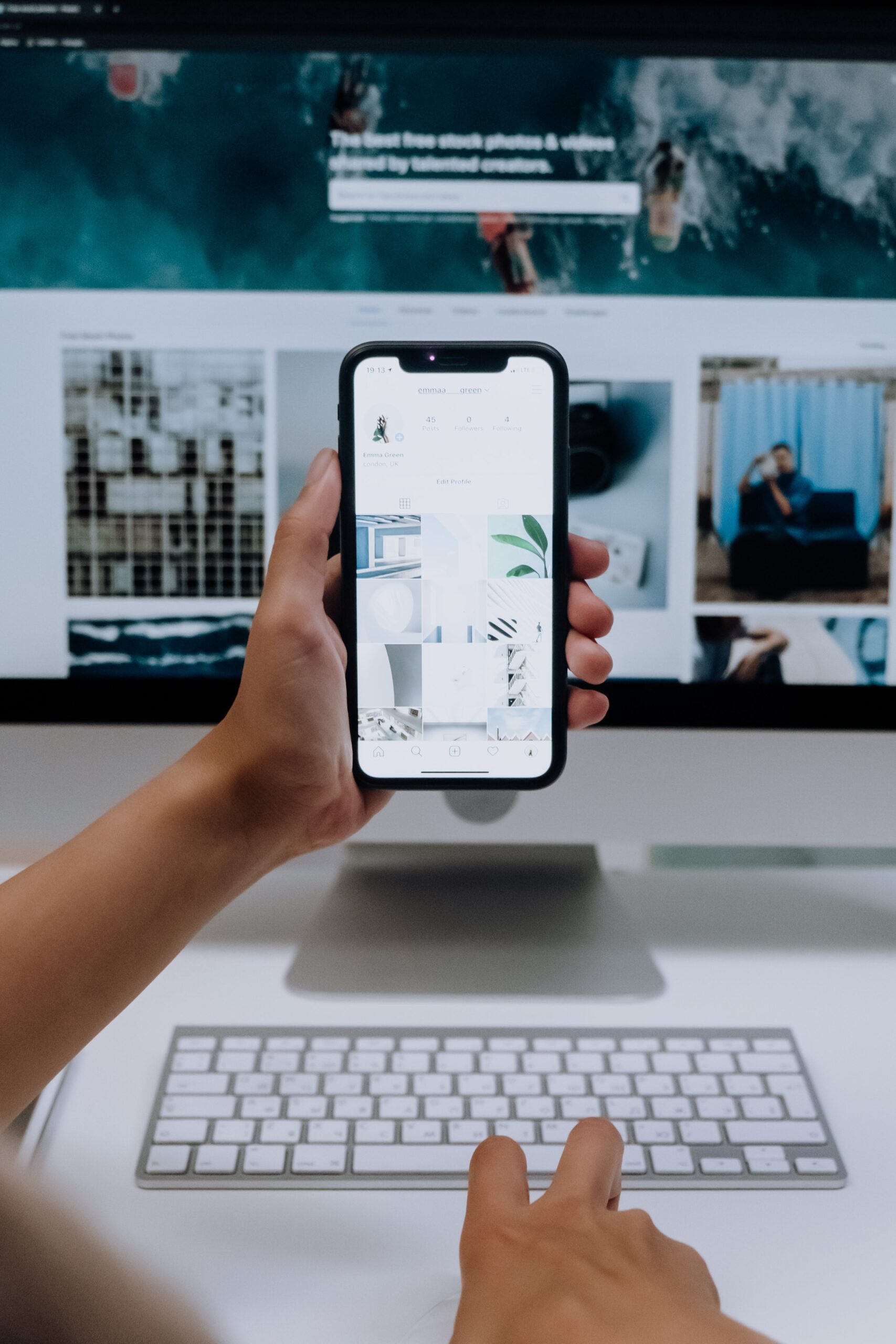 Eine Hand hält ein Smartphone vor einem Computer mit Fotodatenbank